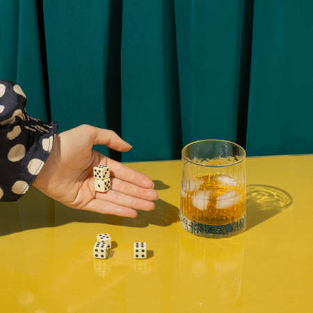 Creative arrangement made of playing dices, a glass and a woman's hand on a yellow table and green curtains. Minimal drinking concept. Party, gambling and elegance inspiration.の写真素材