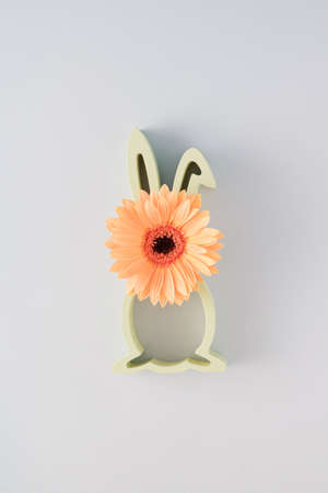 Creative Easter arrangement made of silhouette of a rabbit and an orange gerbera flower on a gray background. Minimal spring concept.の写真素材