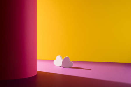 A creative love arrangement made of two white hearts on a yellow and pink background. Minimal shadow...