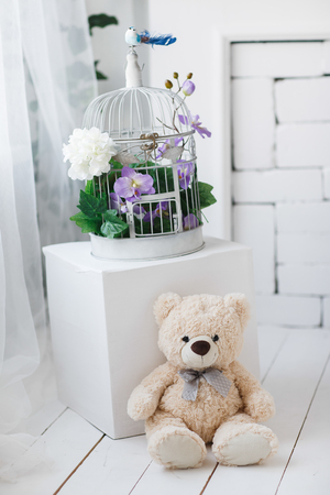 Teddy bear sits on a wooden floor. Spring flowers in the cage.の写真素材