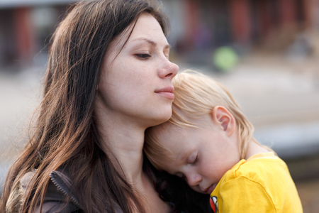 The boy in the yellow shirt is sleeping on mom. Mom looks thoughtfully into the distance.の写真素材