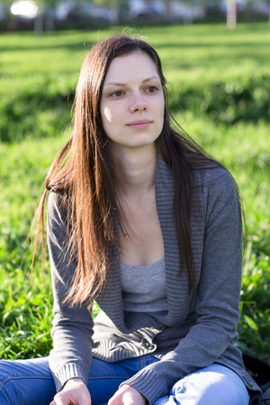 Young beautiful girl sitting on the grass on a sunny day and dreams.の写真素材