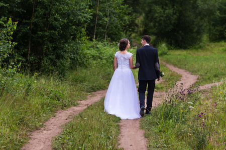Beautiful and happy bride and groom walking in summer forest. Young wedding couple.の写真素材