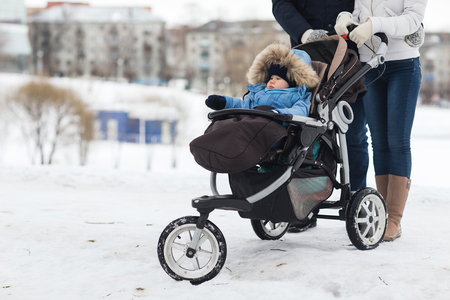 Happy young family walking in the park in winter. The parents carry the baby in a stroller through the snow.の写真素材