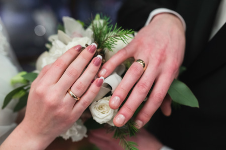 Wedding rings on the hands of the newlyweds. Luxury wedding rings on the hands of the bride and groom on the background of the bouquet.の写真素材