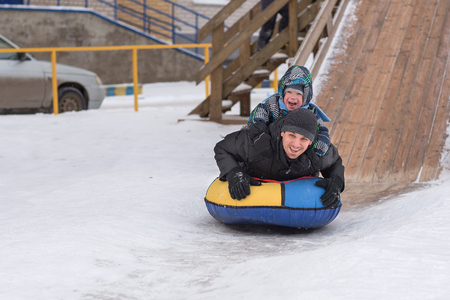 A young man with a cheerful boy with a roller coaster ride in the winter on the ice. Handsome Dad and son laughing in a winter park. Happy family playing with snow.の写真素材