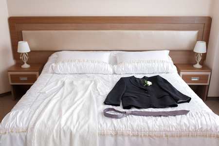 Wedding dress and suit lying on a bed in a hotel room.の写真素材
