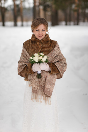 Portrait of a beautiful bride in winter coat with a wedding bouquet.の写真素材