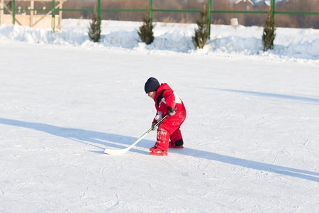 Happy funny kids playing hockey at the rink in the winter. A child with a stick on the ice skating in the winter walks on the street.の写真素材