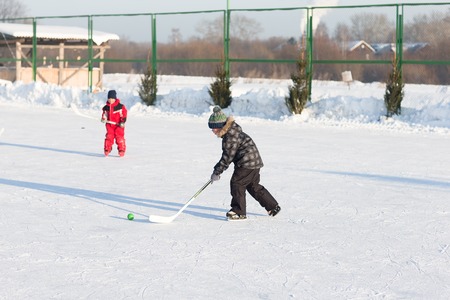 Happy funny kids playing hockey at the rink in the winter. A child with a stick on the ice skating...