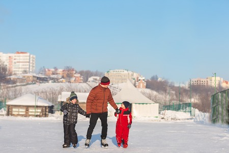 Happy young family skate at the rink in the winter. Beautiful family walking and playing on the ice in winter.の写真素材