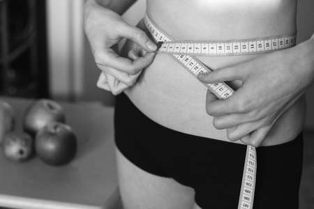 Slim girl with measuring tape in hand. Young beautiful woman measures the his waist.の写真素材