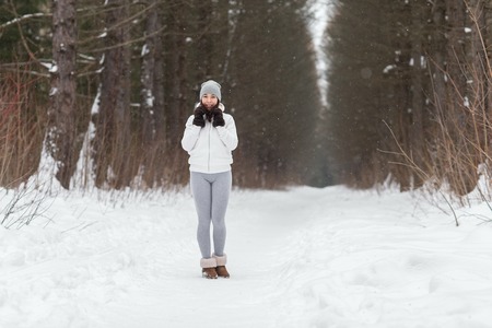 Young athletic woman running around in the woods in winter. Beautiful girl engaged in fitness in winter park.の写真素材