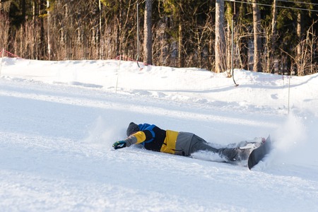 Falling snowboarder downhill. Male snowboarder laying turns on the ski slope. Snowboarder coming down from the mountains in the winter and fall.の写真素材