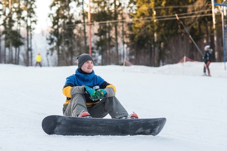 Male snowboarder walking in a winter day on the hill in the woods. Portrait of a snowboarder in the mountains in winter on the ski slope.の写真素材