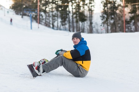 Male snowboarder walking in a winter day on the hill in the woods. Portrait of a snowboarder in the mountains in winter on the ski slope.の写真素材