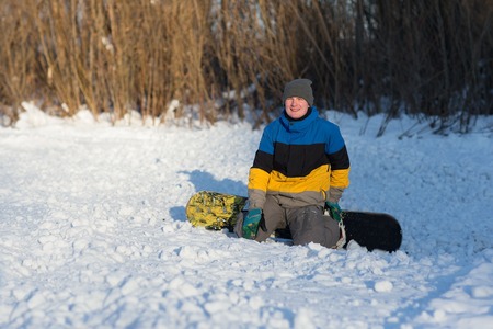 Male snowboarder walking in a winter day on the hill in the woods. Portrait of a snowboarder in the mountains in winter on the ski slope.の写真素材