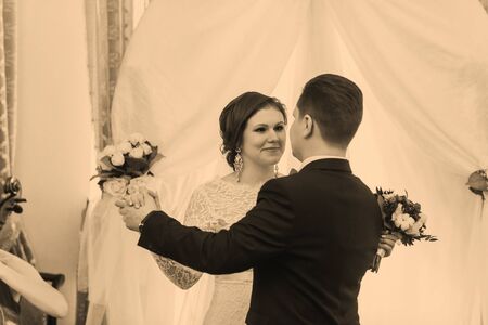 girl in a white wedding dress and bearded man in suit and hat standing near the ceremonial archesの写真素材