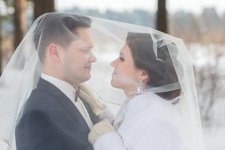Young couple newlyweds walking in a winter forest in the snow. Bride and groom hugging in the park in winter. Beautiful man and woman in their wedding clothes are among the pines.の写真素材