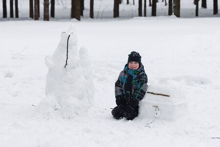 A child enjoys the winter and playing with snow outdoors. The joy and happiness of the boy in the winter forest.の写真素材