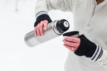 Beautiful Young Woman pours and drinks tea from a thermos after jogging in the winter forest. Trees in the snow. Weather snow cloud. Fitness on the street in the winter.の写真素材