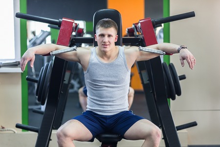 Portrait of a strong fit young man exercising in a gym. Confident man looks ahead.