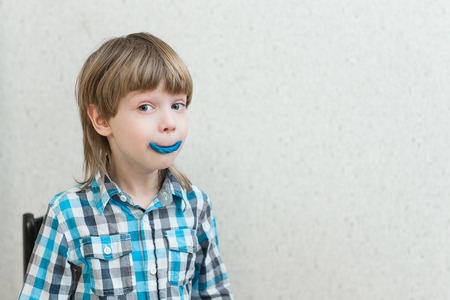 Blond boy put sculpts from clay on mouth at homeの写真素材