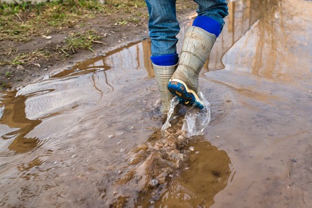 Child wearing rain boots walk into a puddle. Close upの写真素材