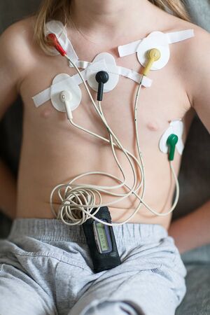 Child sitting on the sofa with Heart cardiogram or monitoring of cardiac performance using Holter.の写真素材