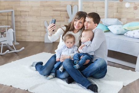 happy parents and little boys twin taking selfie by smartphone in roomの写真素材