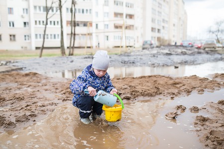 Boy playing with a shovel and bucket in a muddy puddle. Child building sand in the playground.の写真素材