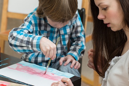 Young beautiful mother with boys son paint colors at home. Mom teaches son to paint colors.の写真素材