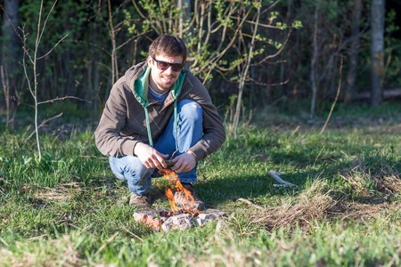 Young sporty and confident man at a picnic by the bonfire next to the wood.