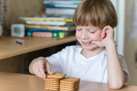 child in the kitchen sitting at the table and eating cookies in the shape of a rectangle.の写真素材