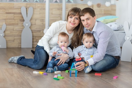 Happy young family of father, mother and twins are built of wooden planks toy house.の写真素材