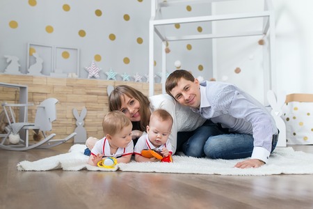 Funny baby boy twins playing on the floor at children, happy parents sitting in the background.