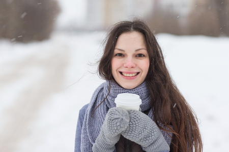 Woman smiling holding hot drink outside in the snowの写真素材