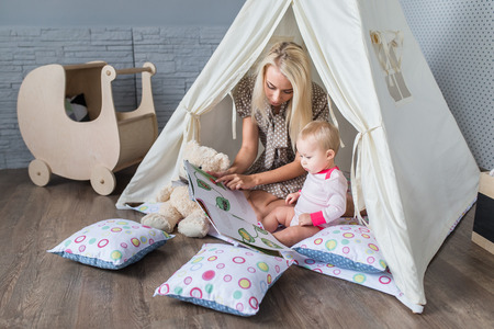 Parents play with children in a teepee tent in the bright nursery.