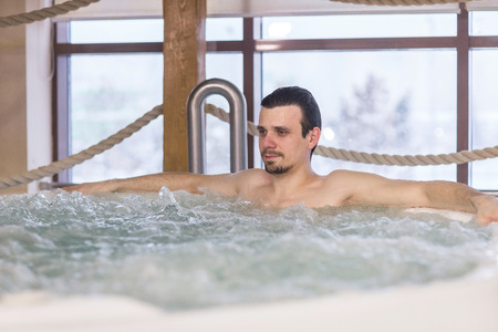 Confident handsome man relax in the tub with hydro massage in Spa salon