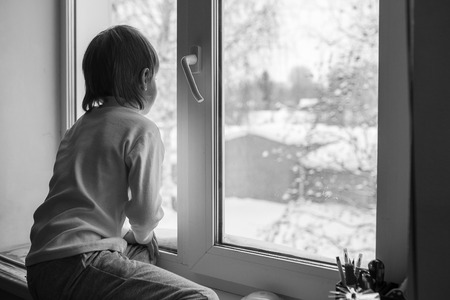 boy looks out the window on a winter dayの写真素材