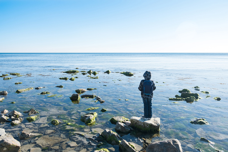 A boy stands on a rock in the black sea and looks out at the waterの写真素材