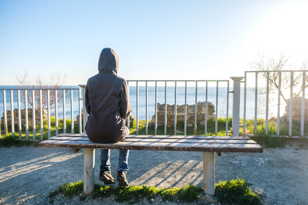 Girl sitting on a red bench facing sea in springtimeの写真素材