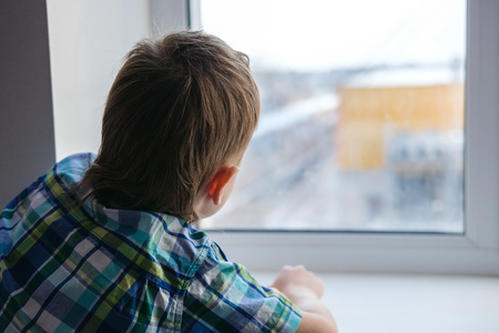 Close up view of little boy looking out of windowの写真素材