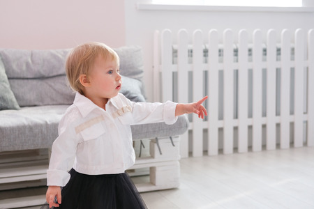 First steps of baby girl learning to walk in white sunny bedroomの写真素材