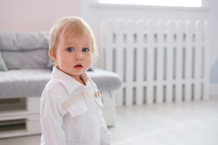 First steps of baby girl learning to walk in white sunny bedroomの写真素材