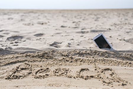 Mobile touch phone in sand on a beachの写真素材