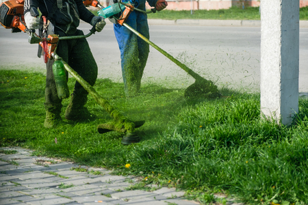 Man wearing overalls and rubber boots mowing green grass with gasoline lawn trimmer.の写真素材