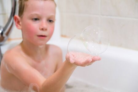 a child plays in a bathtub with soap bubbles at homeの写真素材