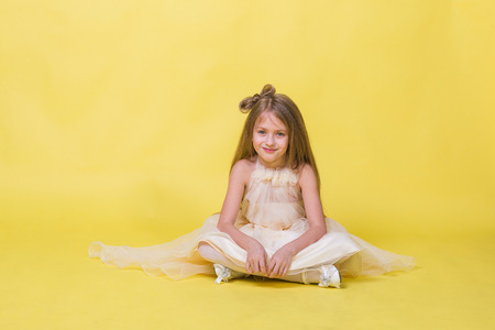 Teenager girl in a dress on a yellow background posing for the camera and sits on the floorの写真素材