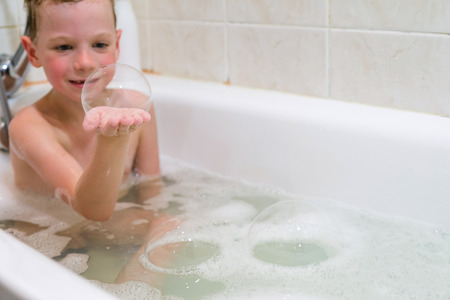 a child plays in a bathtub with soap bubbles at homeの写真素材
